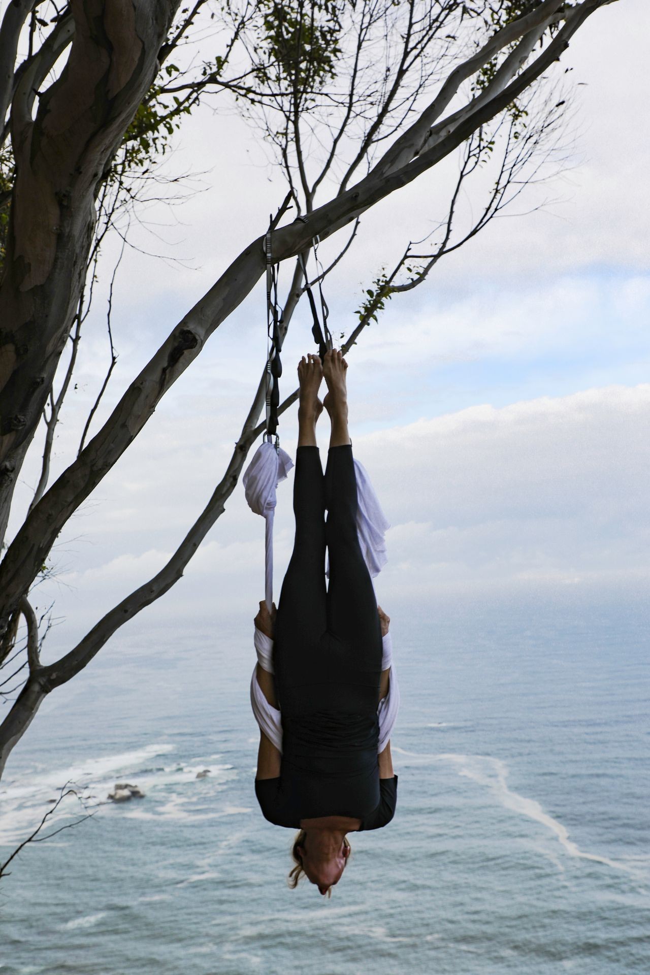 Person hanging upside down in aerial silks with ocean background.